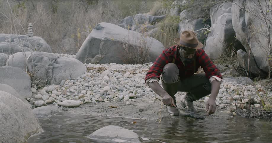 A black man pans for gold in a stream