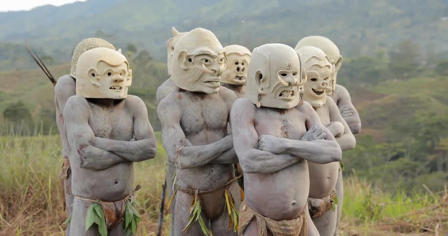 A group of painted tribal men with masks stand outside clustered together