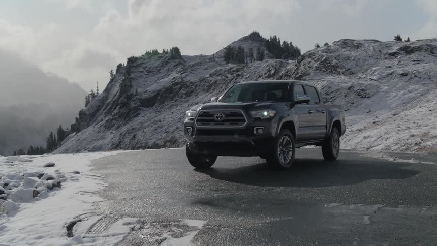 A grey toyota truck driving up a hill and coming to a stop on a cloudy winter day surrounded by snowy mountains