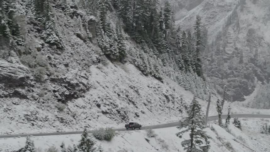 A pickup truck driving through twisting roads surrounded by snow covered mountains and trees