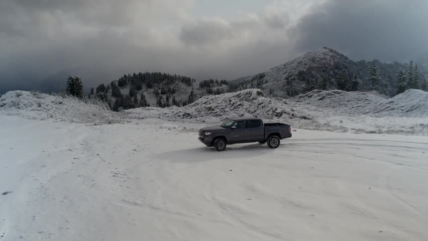 A pickup truck driving to a stop in a large snow covered lot in the mountains