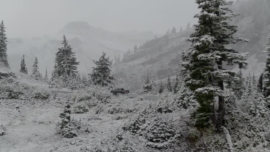 A car drives through falling snow in the mountains