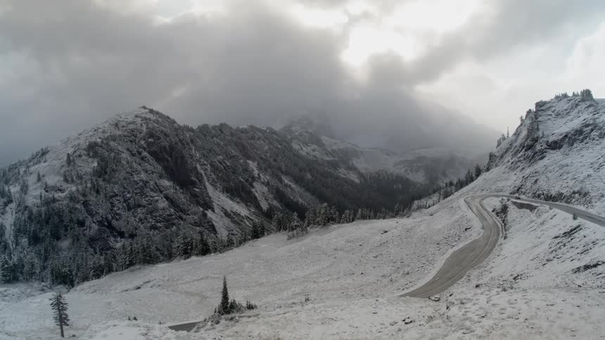 Flying over a road that is in a snowy mountain range