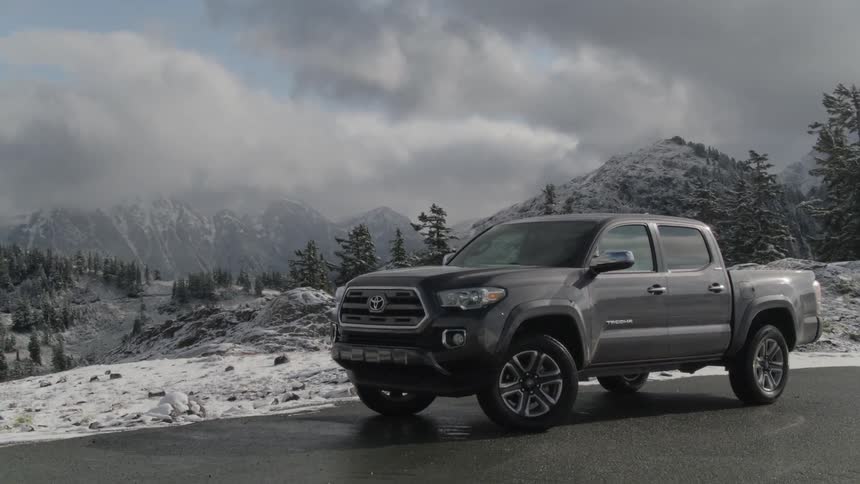 A pickup truck on the road with trees and mountains in the background