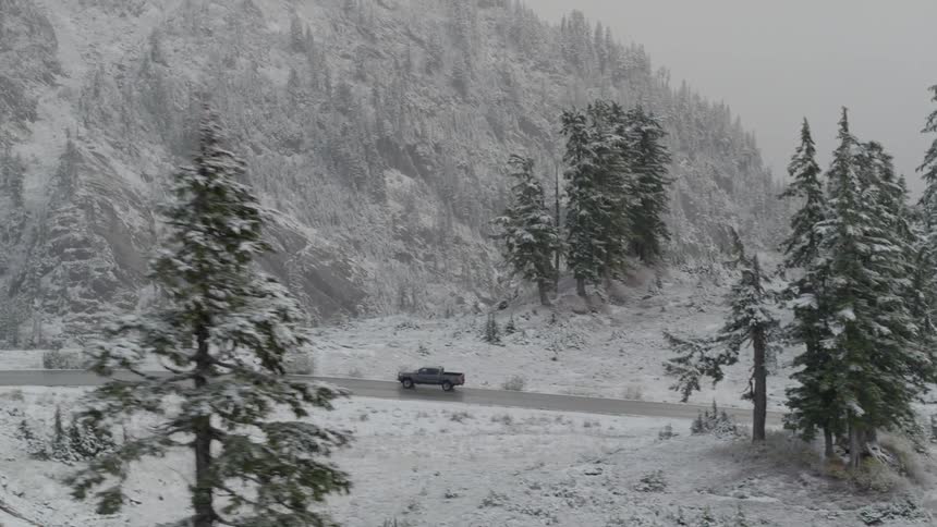 A pickup travels on a curving mountain road in the snow on a foggy day