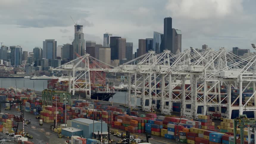 Thousands of shipping containers on a commercial dockyard fitted with cranes with a city skyline across the river