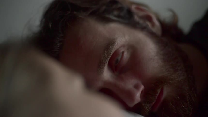 A man with a beard looks at a woman while lying in bed