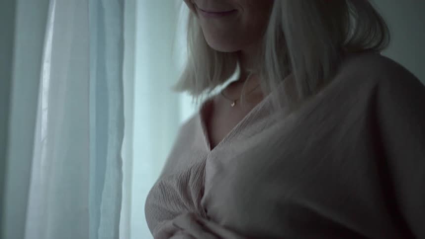 A pregnant white woman rubs her stomach and slightly smiles