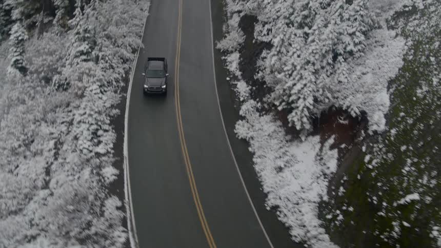 A truck drives down a winding road surrounded by snow covered trees and hills