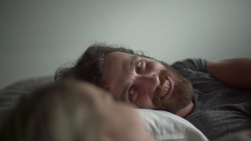 A man smiles at another person with his head laying on a pillow