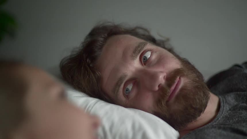 A man winks at the woman laying beside him in bed