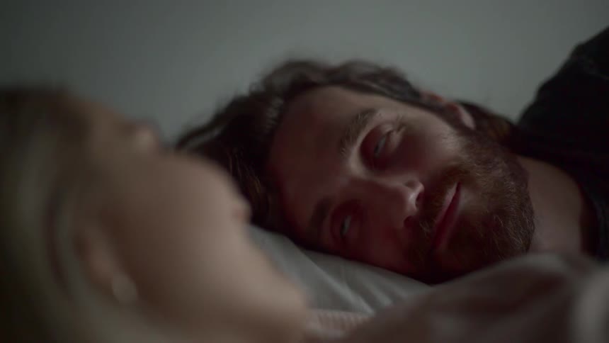 A man smiles and stares at the woman laying next to him in bed