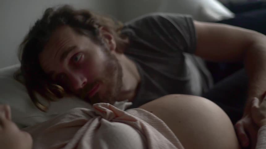A man placing his head on a pregnant womans stomach then looking at her and smiling