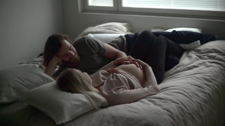 A man lays with a pregnant woman in bed