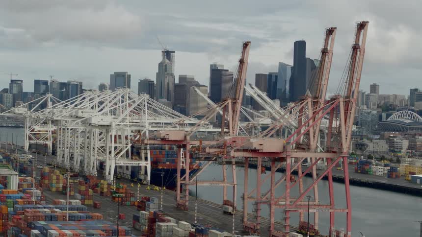 Cargo containers sit by loading cranes at a dock