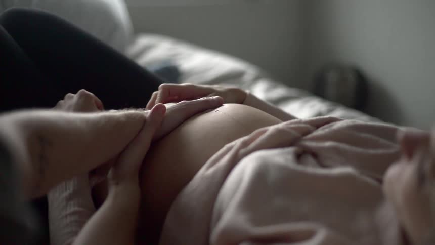 A pregnant woman laying down as a man rubs her bare belly