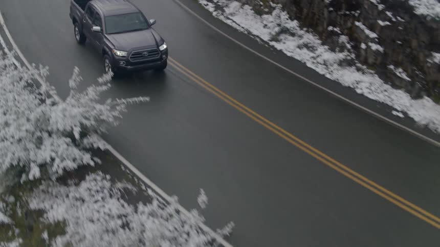 A black pickup truck following a curved road on a snowy mountain