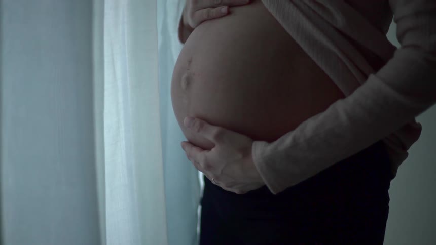 A pregnant woman rubs her bare stomach