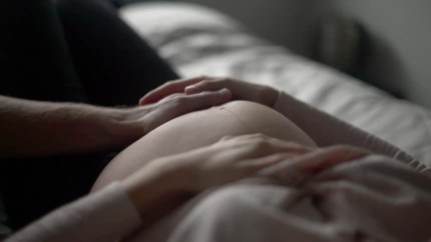 A man and woman hold hands over a womans pregnant stomach
