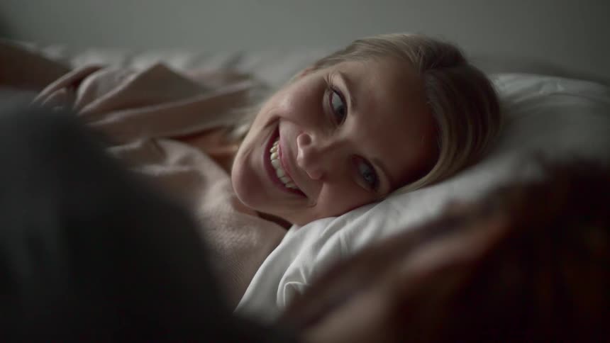 A white woman turns her head on a pillow and smiles