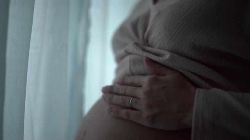 A woman looks down and smiles as she lovingly caresses her pregnant belly