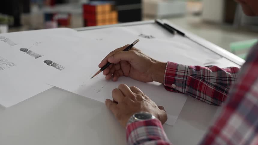 A man uses a pencil to draw at a drafting desk