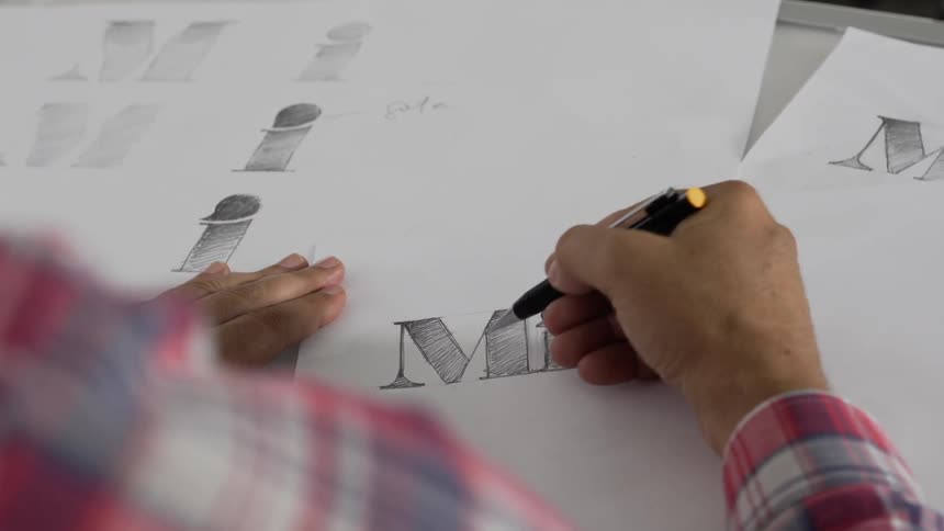 An artist is inking in lines on lettering inside in daylight