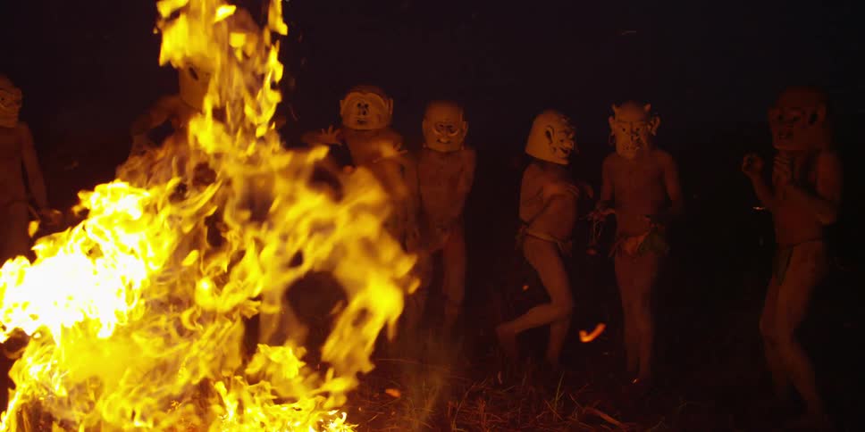 People wearing mask dancing around a fire