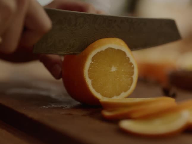 A white person carefully cuts an orange with a knife