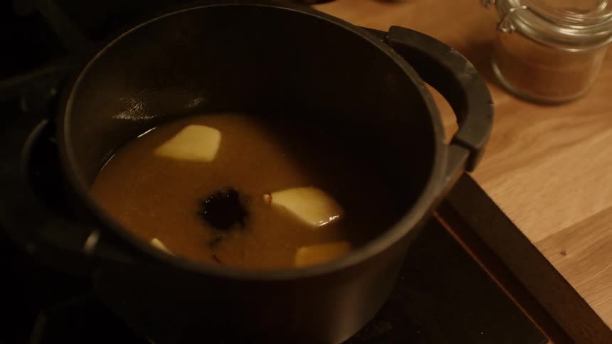 A person adding two spoonfuls of chocolate into a pot with melted butter
