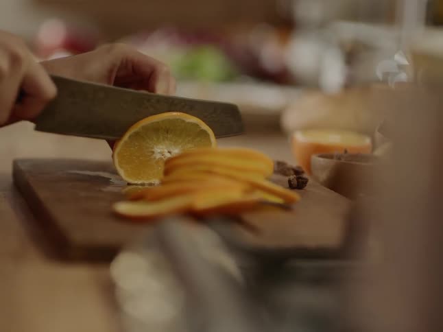 A woman uses a knife to cut an orange on a wood cutting board in a kitchen
