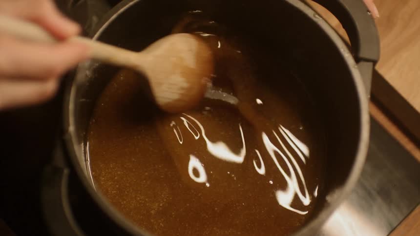 A brown sauce being stirred with a wooden spoon