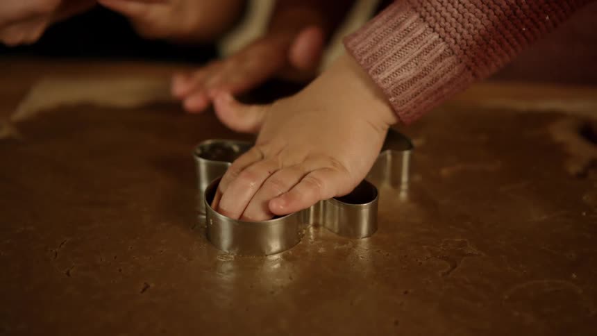 A child presses a cookie cutter onto dough to make gingerbread cookies