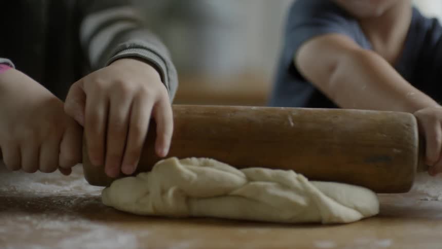A pair of children smoothing dough with a wooden rolling pin