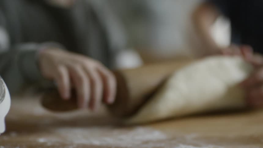 Two white children roll a rolling pin over a piece of dough