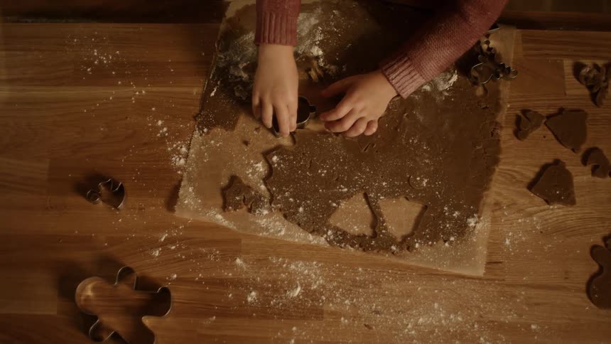 A child cutting out gingerbread cookies with a nearby adult