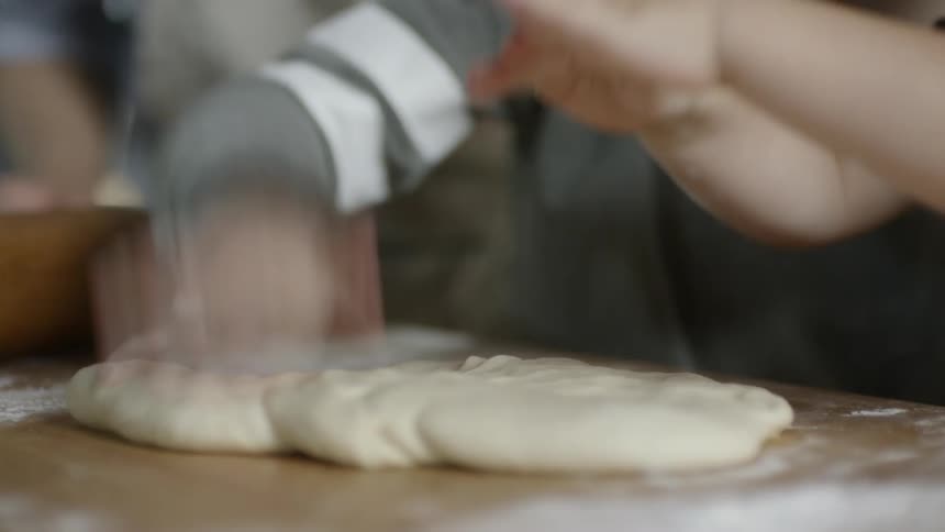 Two kids flatten and hit dough sitting on a countertop