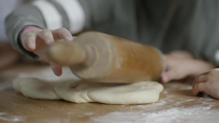 A child rolls out dough on a kitchen counter covered with flour