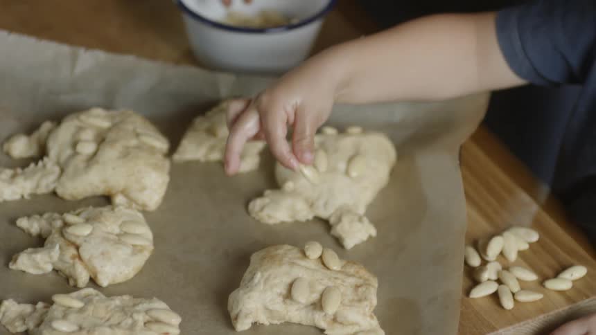 Children press almonds onto pastry dough on a parchment paper lined cookie sheet