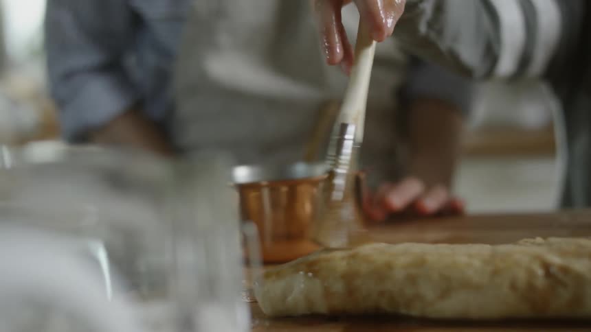 A person using a paint brush to brush sauce on dough
