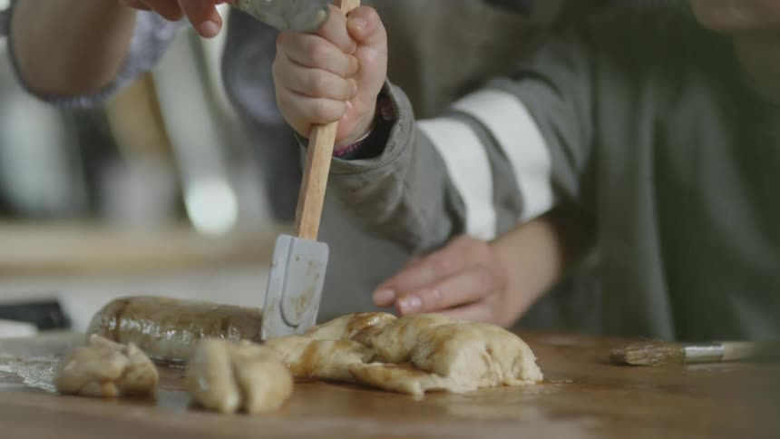 A child pulls a spatula through and slices rolled dough on a cutting board with the guidance of an adult