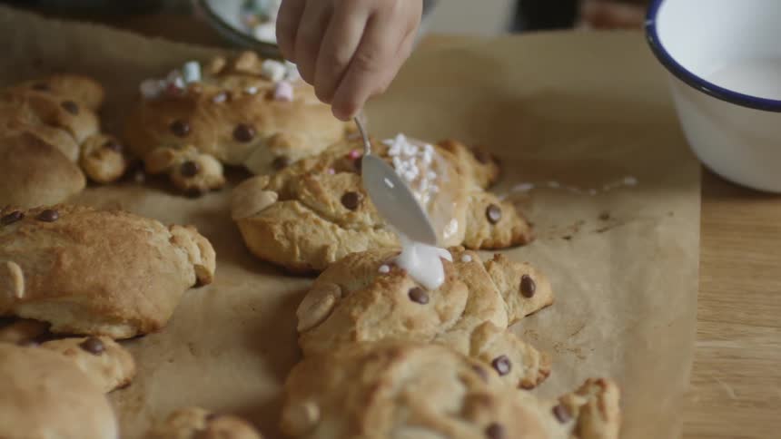 A white child carefully drizzles white cream on top of a chocolate chip cookie