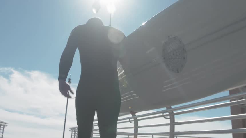 Surfer walks along a dock on a sunny day