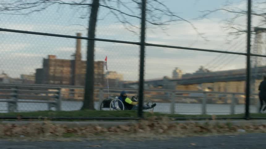 Man riding a hand bike passes a jogger