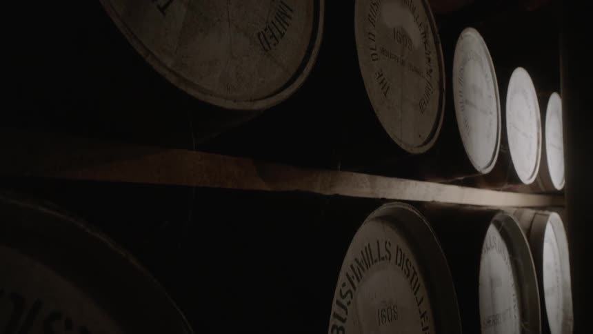 Barrels of bourbon sit on wood shelves in a distillery