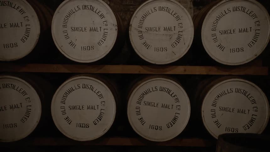 Barrels of single malt whiskey sit on wood shelves in a distillery