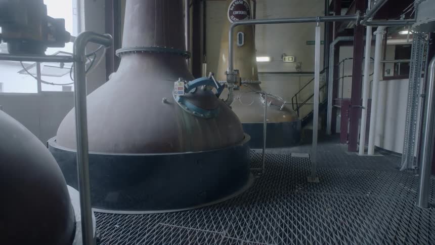 Large brewing vats in a factory with metal floors pipes and large windows