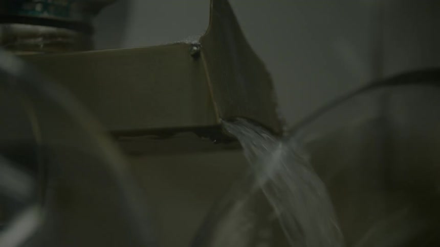Water running out of a tap and into a glass container