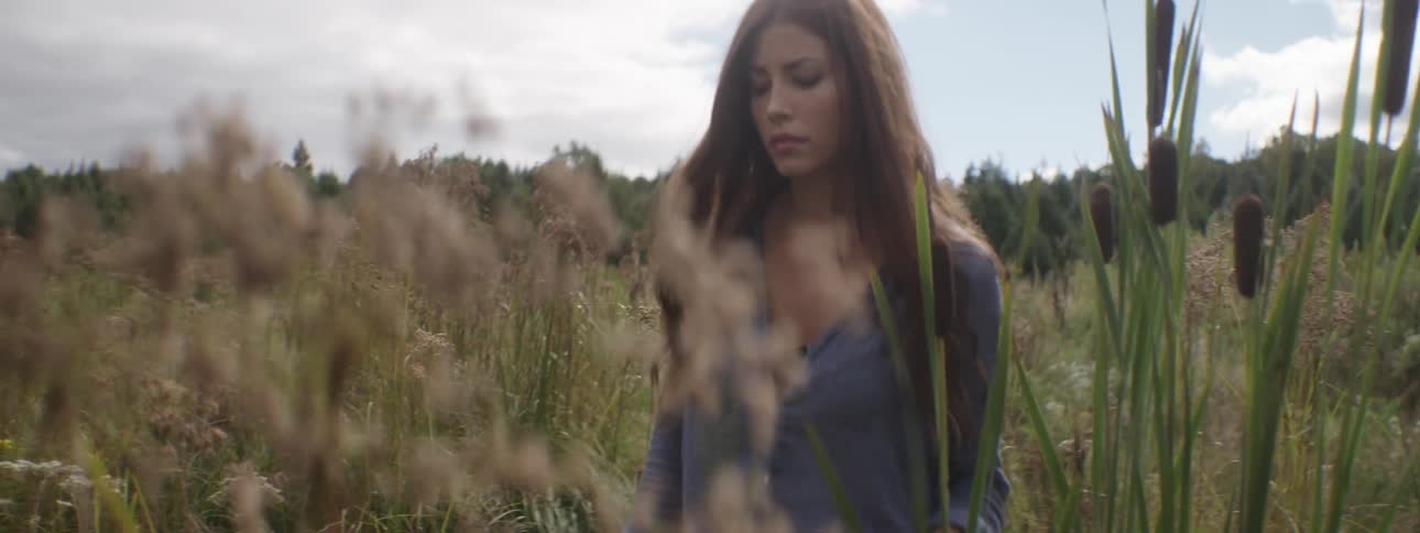 A young woman makes her way through the tall grass and plants of a clearing in a forest
