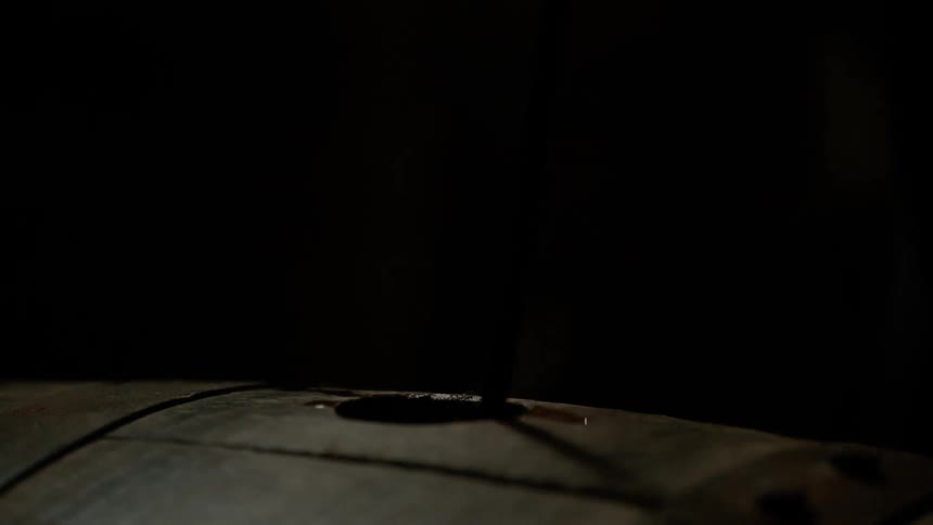 A ladle is lowered into a hole in a wood barrel
